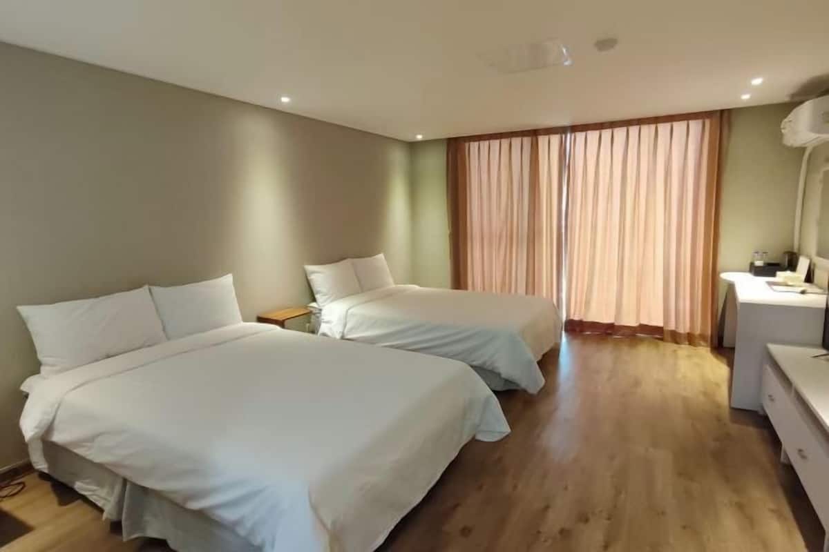 Quarto de hotel com duas camas, uma escrivaninha, uma cadeira e uma janela com cortinas.
