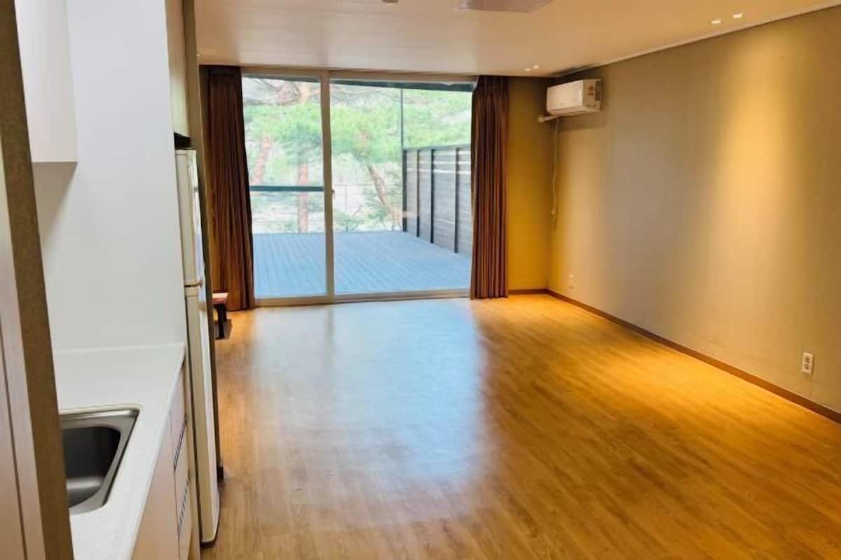 Um quarto espaçoso com piso de madeira, uma porta de vidro deslizante que dá para uma área externa e um ar condicionado instalado na parede.