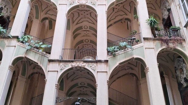 Edifici d'altes plantes amb detalls arquitectònics ornamentals, incloent balcons arquejats i motius decoratius al sostre.