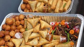 Dos bandejas de samosas y otros bocadillos, cada una acompañada de un recipiente con salsa.