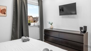 Habitación de hotel moderna con una cama grande, un aparador de madera oscura, un televisor de pantalla plana montado en la pared y una ventana con cortinas.