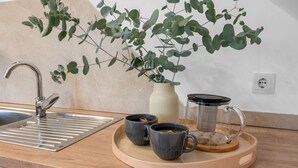 Una encimera de cocina con un fregadero, dos tazas, una planta y una cafetera.