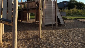 Estructura de madera para juegos infantiles con un tobogán y elementos de escalada, rodeada de grava.
