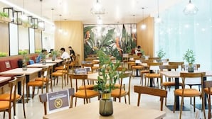 A spacious restaurant with multiple tables and chairs, a large mural on the wall, and hanging pendant lights. - Cordia Hotel Yogyakarta - Airport Hotel (Temon)