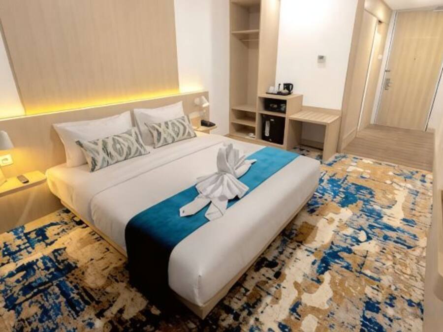 Una habitación de hotel con cama, mesita de noche y vestidor.