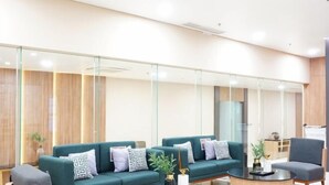 A modern lobby with a teal sofa set, round coffee tables, and glass partitions. - Cordia Hotel Yogyakarta - Airport Hotel (Temon)