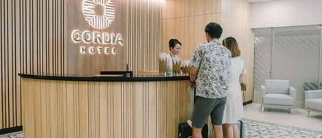 A reception desk with a logo, a check-in counter, and a seating area with chairs.