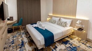 Ein Hotelzimmer mit Bett, Schreibtisch, Stuhl, Fernseher und einem Fenster mit Vorhängen.