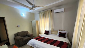 A hotel room with a bed, a desk, a chair, a ceiling fan, and an air conditioning unit. - Laylah Suites and Apartment (Gombe)