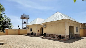 A building with a tiled courtyard and a water tower in the background. - Laylah Suites and Apartment (Gombe)