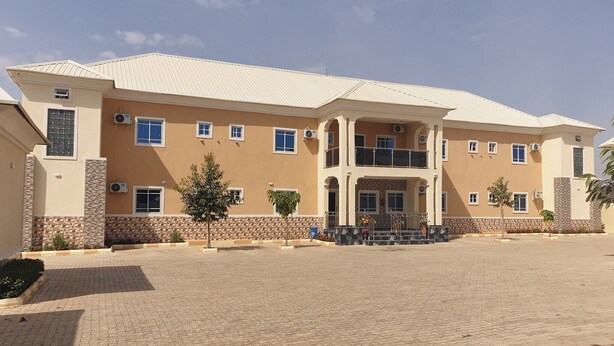 A two-story building with a symmetrical facade, multiple windows, and a central entrance with a staircase. - Laylah Suites and Apartment (Gombe)