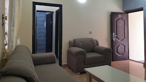 A living room with a sofa, a chair, and a table. There is a door with a window and a light fixture on the ceiling. - Laylah Suites and Apartment (Gombe)