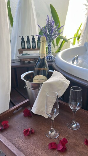 Un plateau avec une bouteille de vin Quinta Brasilis Paraty, deux verres à vin vides et des pétales de rose éparpillés.