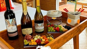 Une table en bois sur laquelle sont disposées trois bouteilles de vin Quinta Brasilis, une assiette de fruits, un gâteau sur un présentoir et un chandelier.