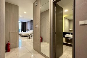Una habitación de hotel con cama, un baño con espejo y lavabo, y un extintor.
