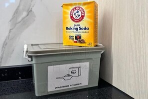Un récipient étiqueté « Lessive », sur lequel repose un sac de « bicarbonate de soude pur ».