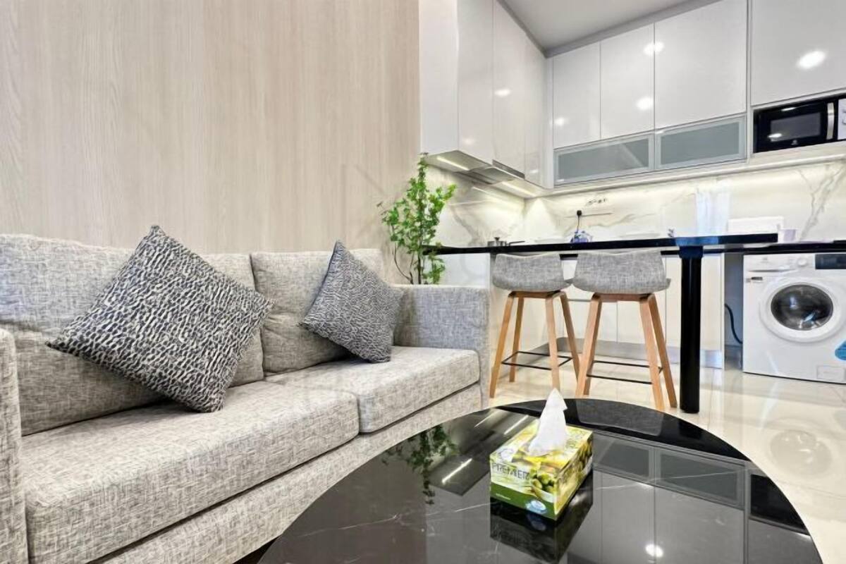 A modern living room with a sofa, a coffee table, and a kitchen area with a washing machine.