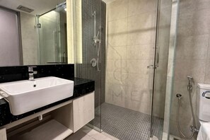 Une salle de bain moderne avec un lavabo blanc, un plan de toilette noir et une douche à parois de verre.