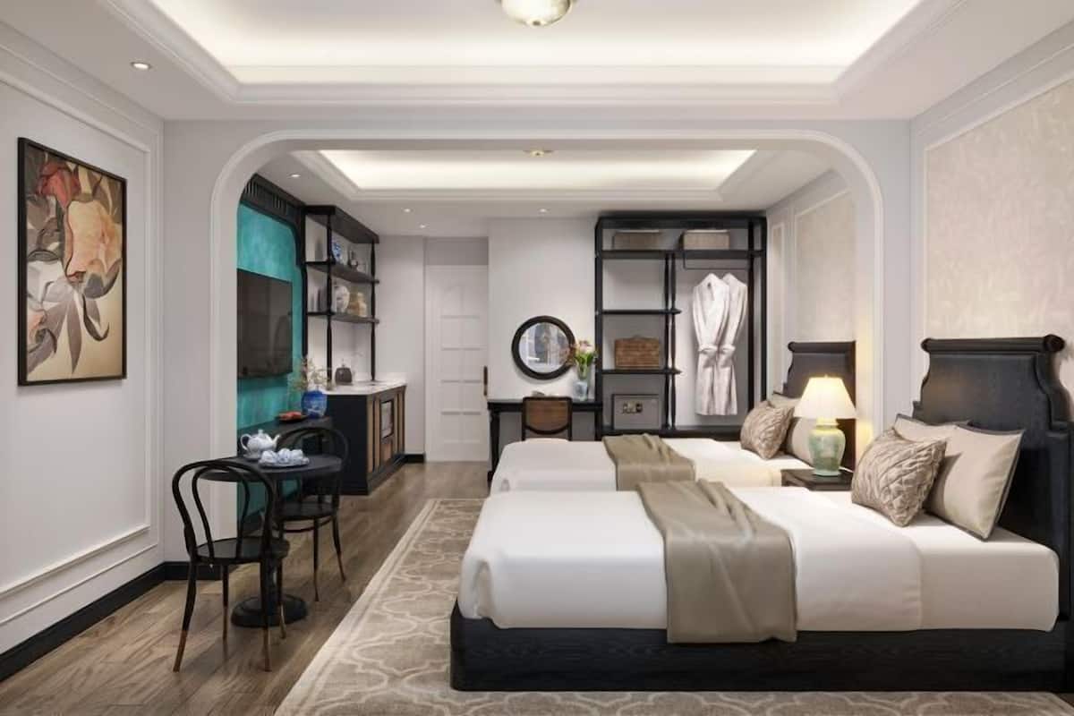 A hotel room with a bed, a desk, a chair, a bookshelf, and a painting on the wall.