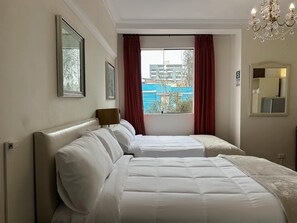A hotel room with two beds, a large window with red curtains, a chandelier, and a view of buildings outside. - Kontiki Miraflores  (Lima)