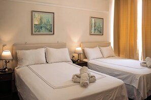 Hotellihuoneessa on kaksi sänkyä, joissa kummassakin on tyyny ja lamppu. Seinällä on kaksi kehystettyä taulua.
