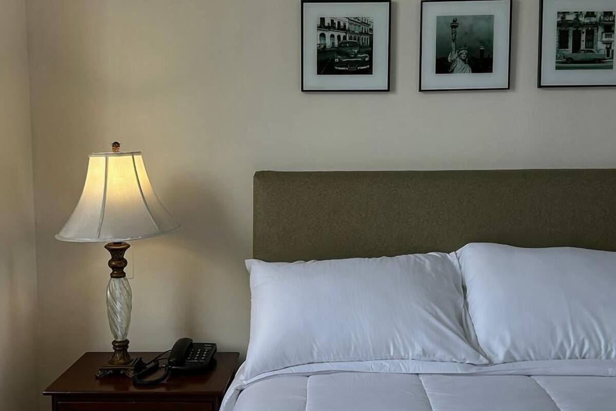A hotel room with a bed, a nightstand with a lamp, and three framed pictures on the wall.