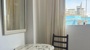 Ein Eckzimmer mit rundem Tisch und Stuhl, einem fenster mit Vorhängen und Blick auf Gebäude.