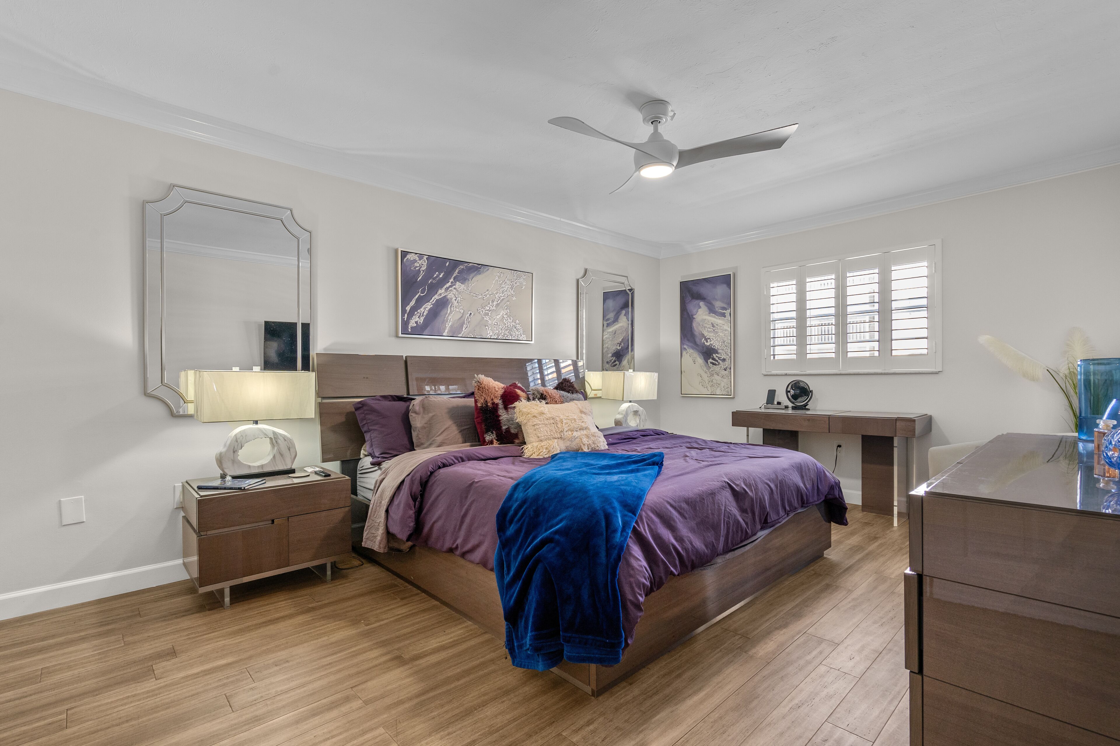Ein Schlafzimmer mit einem Bett, Nachttischen, einer Kommode, einem Deckenventilator und Kunstwerken an den Wänden.