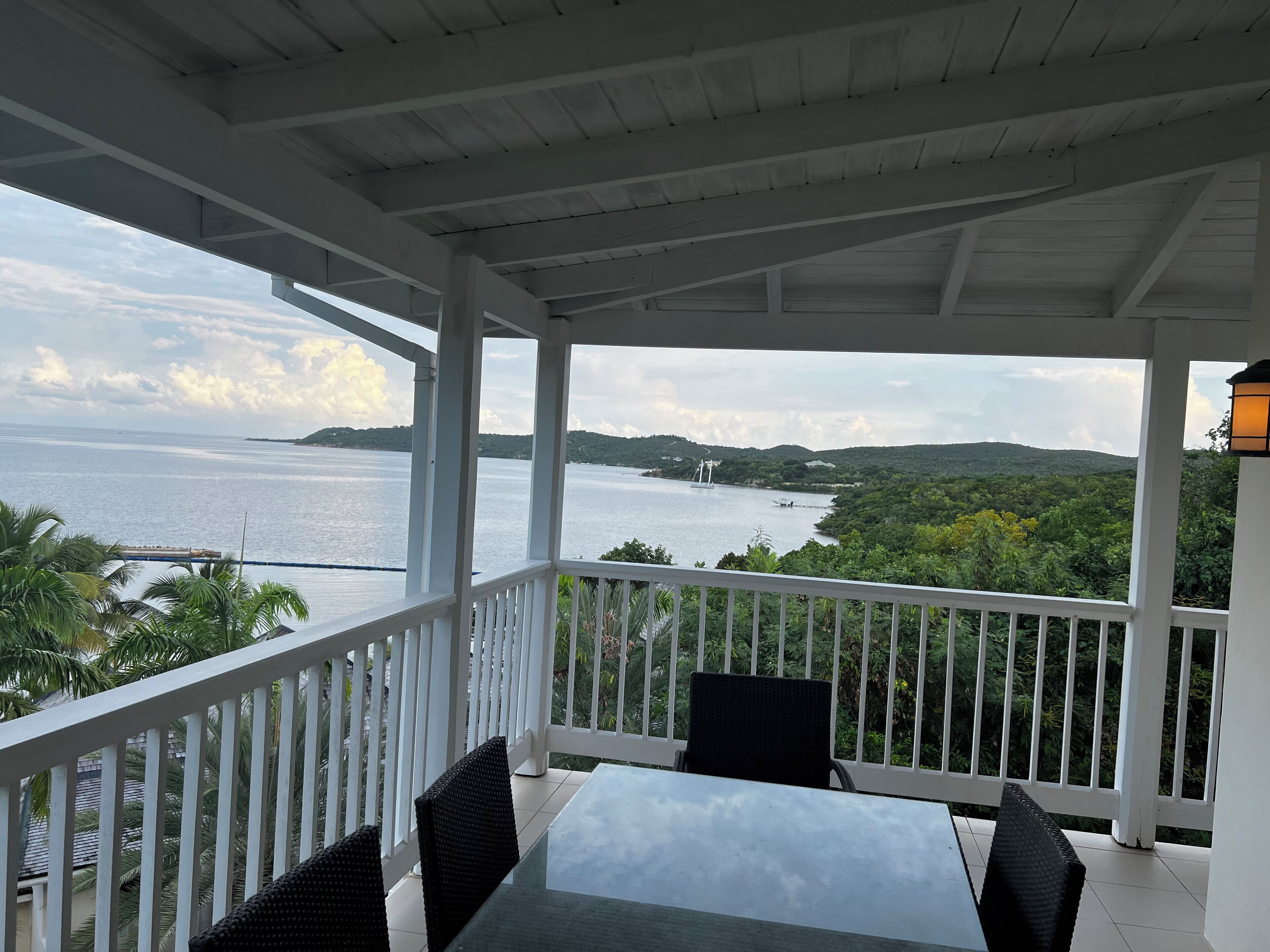 A covered outdoor area with a table and chairs, overlooking a body of water and greenery.