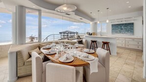 Un comedor moderno con vistas panorámicas al océano, un bar y una cocina con armarios blancos.