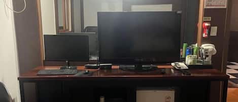 A desk with a computer, a keyboard, a mouse, and a monitor. There is a small refrigerator below the desk.