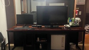A hotel room with a wooden desk, two monitors, a keyboard, a mouse, a telephone, and a small refrigerator. - Sisilli Motel (Uijeongbu)