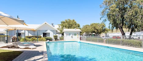 Ein Swimmingpool mit Liegestühlen, einer Rettungswache und einem eingezäunten Bereich mit Bäumen.