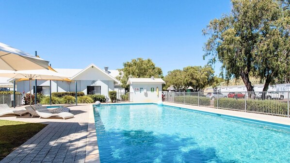 A swimming pool with lounge chairs, a lifeguard station, and a fenced area with trees. - Cape View TwentyTwo – a modern 2-bedroom, 2-bathroom villa (Broadwater)