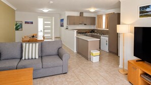 A modern living room with a grey sofa, a small dining table, and a TV stand. - Cape View TwentyTwo – a modern 2-bedroom, 2-bathroom villa (Broadwater)