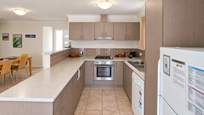 A modern kitchen with a central island, stainless steel appliances, and a dining area with a table and chairs. - Cape View TwentyTwo – a modern 2-bedroom, 2-bathroom villa (Broadwater)