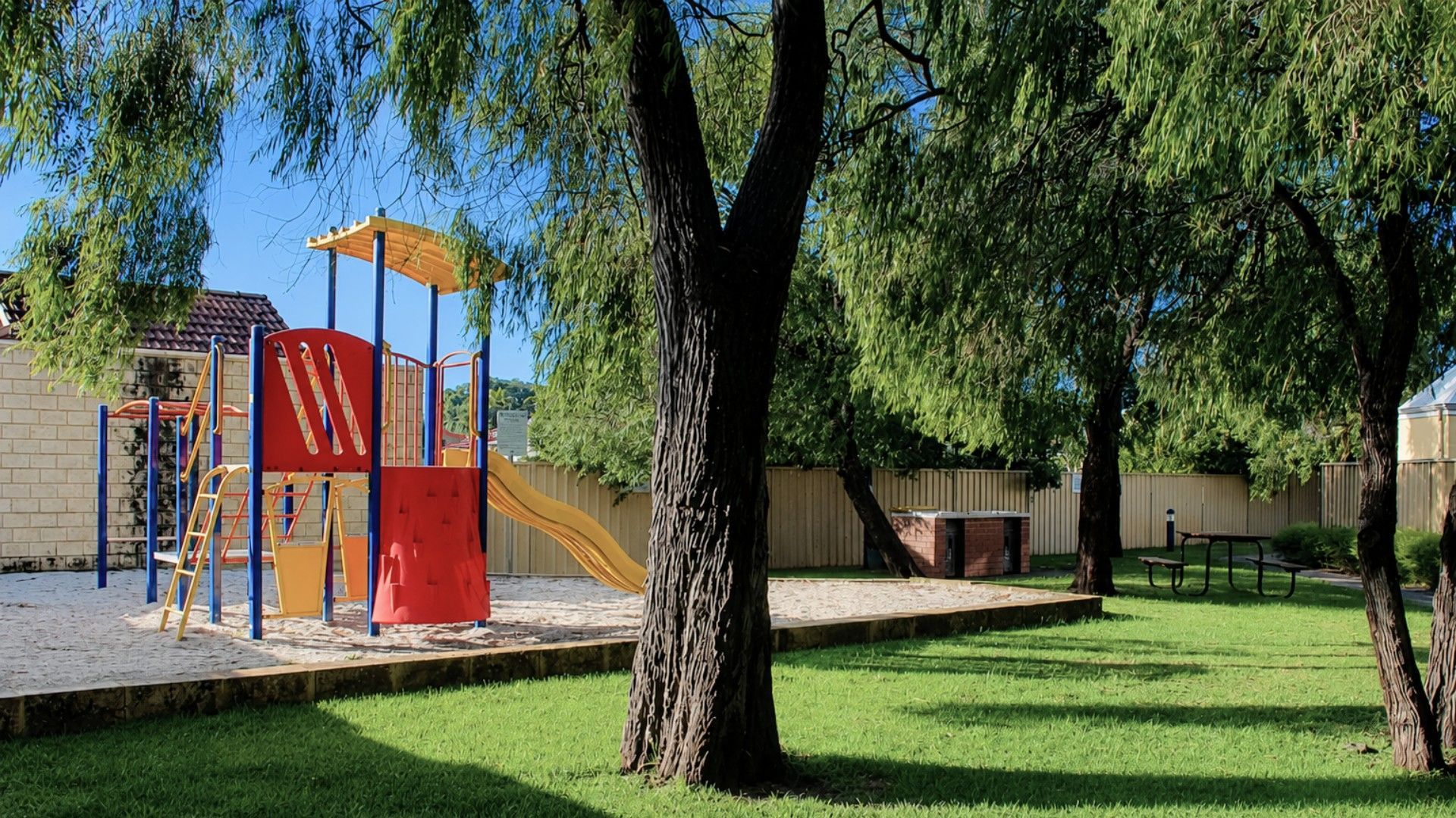 A playground with a slide and climbing structures, surrounded by grass and trees.