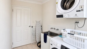 A laundry room with a washing machine, a dryer, a sink, and an ironing board. - Cape View TwentyTwo – a modern 2-bedroom, 2-bathroom villa (Broadwater)