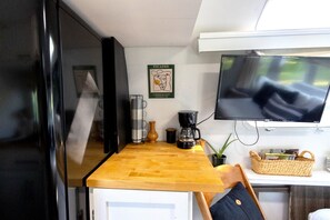 A kitchen with a wooden countertop, a coffee maker, a television mounted on the wall, and a framed artwork. - Riverfront Vintage Trailer on the Guadalupe - Private River Entrance (Canyon Lake)