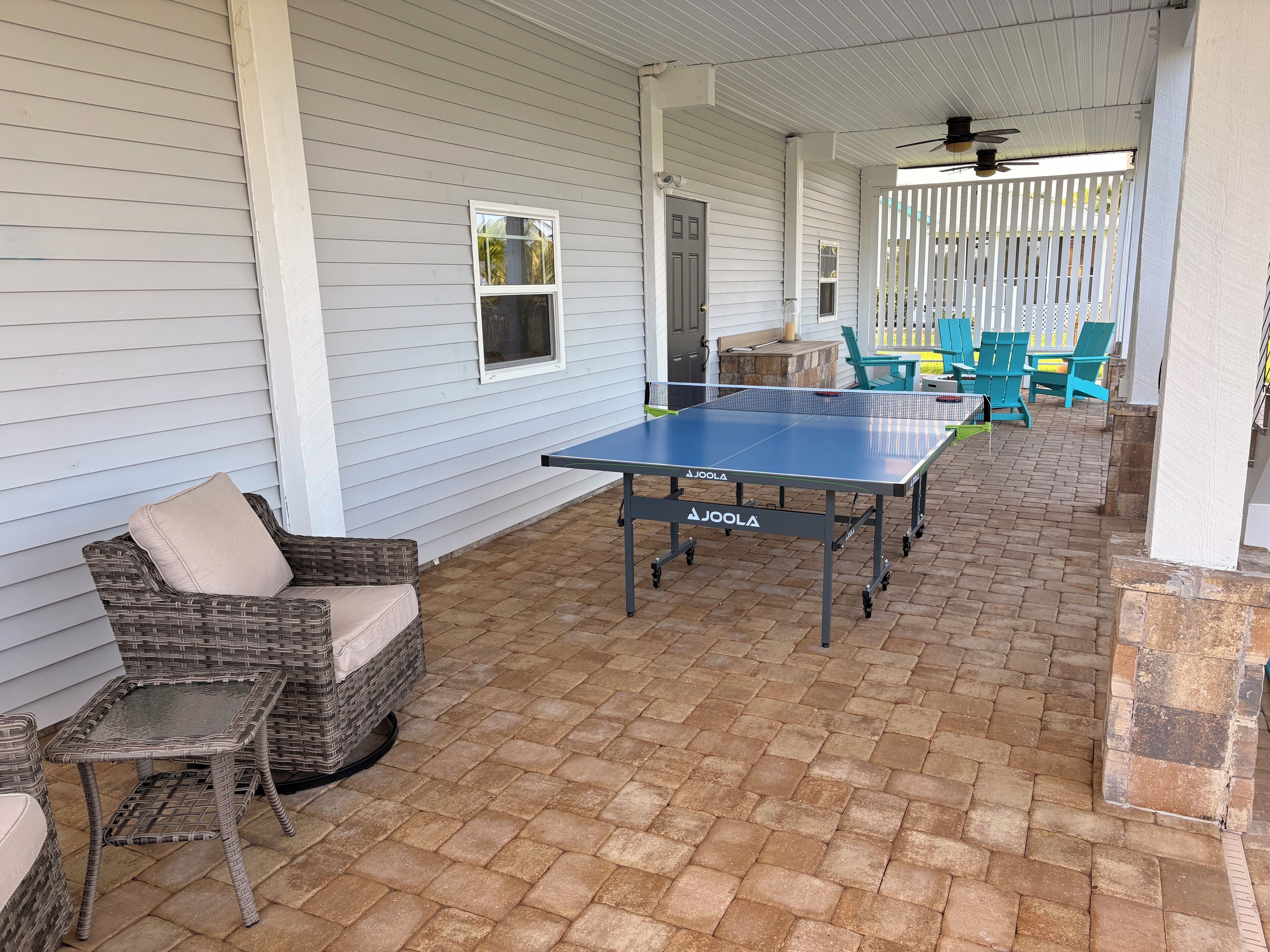 Une terrasse extérieure avec une table de ping-pong, des meubles en osier et un sol en briques.