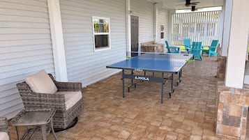 Une terrasse extérieure avec une table de ping-pong, des meubles en osier et un sol en briques.