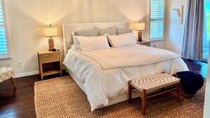 Une chambre à coucher avec un grand lit, deux tables de chevet, un banc et un fauteuil suspendu.