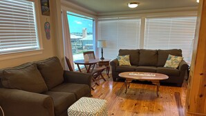 A living room with a brown sofa, a matching ottoman, a wooden coffee table, and a view through large windows. - EAGLES NEST #1 AT SUN PERCH VILLAS. BEAUTIFUL VIEWS OF FALSE RIVER! (Ventress)
