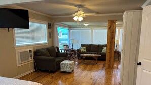 A spacious living room with hardwood floors, a ceiling fan, and a large window with blinds. - EAGLES NEST #1 AT SUN PERCH VILLAS. BEAUTIFUL VIEWS OF FALSE RIVER! (Ventress)