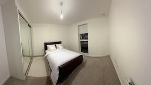 Une chambre à coucher comprenant un lit, une porte-fenêtre coulissante, une fenêtre et un luminaire au plafond.