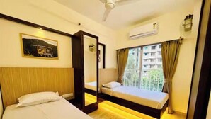 A hotel room with two beds, a large mirror, an air conditioning unit, and a view of a building through the window. - Executive 1BHK Suite | Near Link Road (Mumbai)