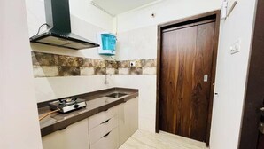 A compact kitchen with a gas stove, a sink, and a wooden door. - Executive 1BHK Suite | Near Link Road (Mumbai)