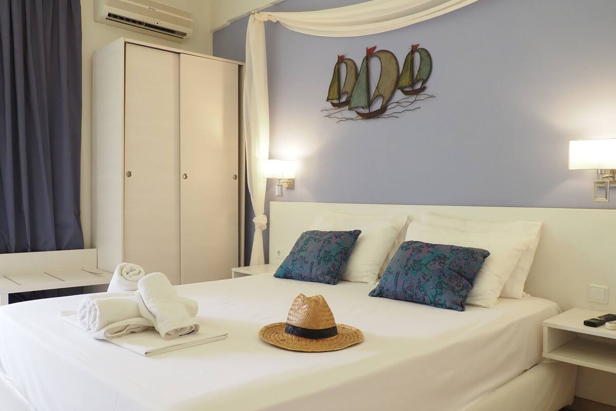 A hotel room with a bed, a nightstand, a wardrobe, and a wall-mounted artwork of sailboats.