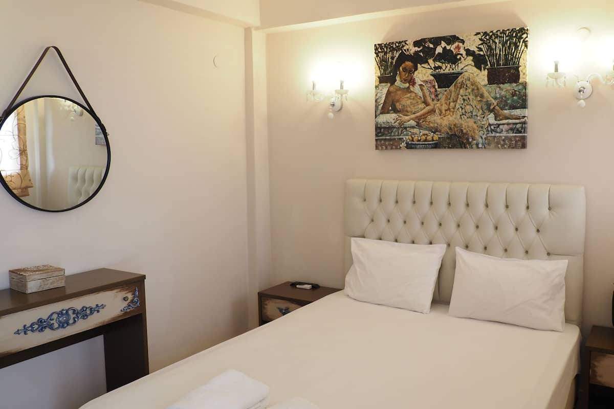 A neatly made bed with a tufted headboard, a bedside table with a vase, and a wall-mounted painting.