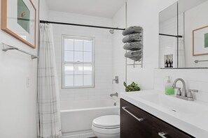 Une salle de bain moderne avec une baignoire blanche, des toilettes et un lavabo surmonté d’un miroir.
